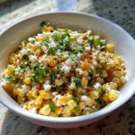 A close-up bowl of vibrant Mexican Street Corn Salad topped with cotija cheese, cilantro, and chili powder.