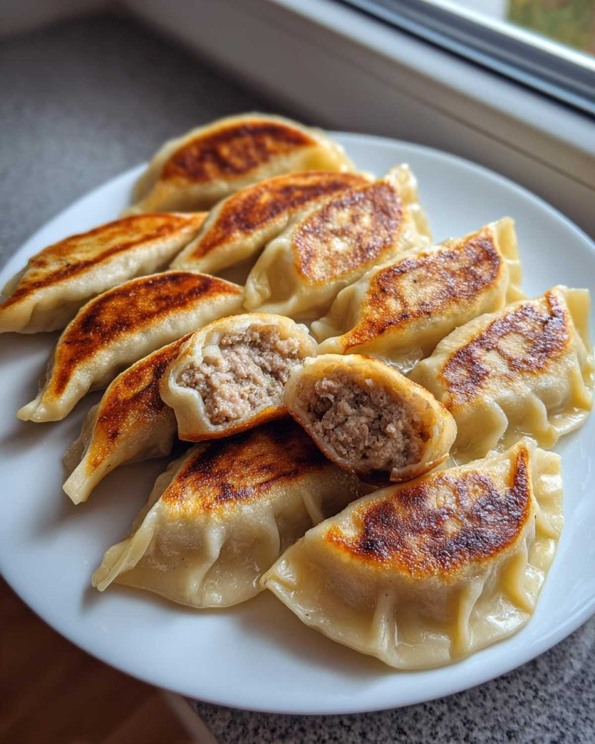 A plate of pan-fried dumplings, showing a crispy golden bottom and one dumpling cut open to reveal the savory meat filling.