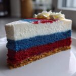 A perfect slice of Red White and Blue Cheesecake showing distinct red, blue, and white layers on a graham cracker crust.