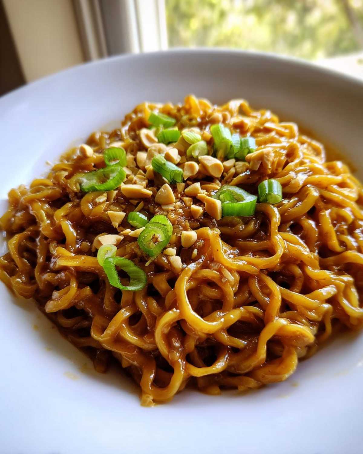 A close-up shot of glossy, saucy ramen noodles topped with chopped peanuts and bright green scallions.