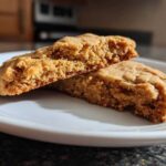 Close-up of a soft Peanut Butter Cookies broken in half, showing the chewy interior texture on a white plate.