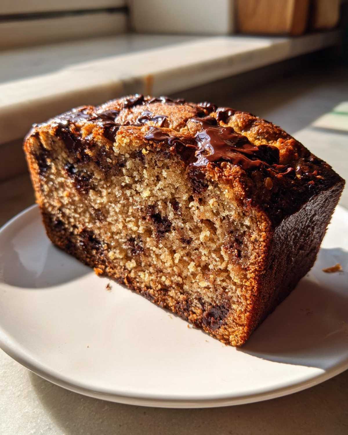 A close-up slice of Sourdough Chocolate Chip Quick Bread with melted chocolate drizzled on top, sitting on a white plate.